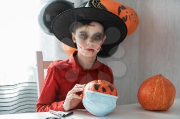 Teen boy in costume and face masks to protect against COVID-19 drawing a pumpkin for the Halloween celebration. Halloween carnival with new reality with pandemic concept.