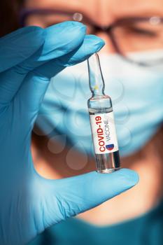 Coronavirus Russia-developed vaccine concept: vaccine with Russia flag in doctor hand with blue protective gloves.