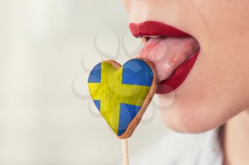 Closeup photo of the woman lips and cookie hearts with flag of Sweden