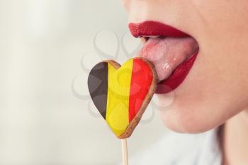 Closeup photo of the woman lips and cookie hearts with flag of Belgium