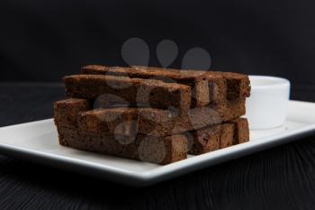 Crackers with garlic from black bread in oil on a wooden black background.