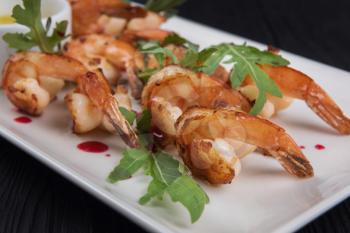 Fried shrimps with sauce and arugula on plate