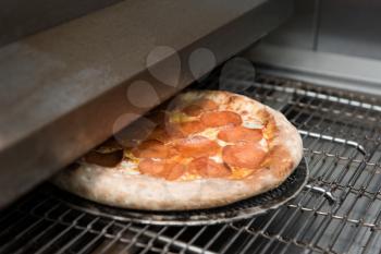 Preparing pizza in oven at restaurant kitchen, ready pizza from electric conveyor oven