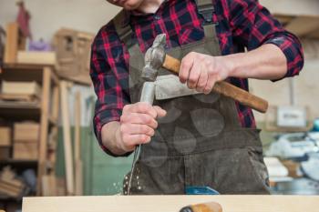 Carpenter working with a chisel and hammer in a wooden workshop. Profession, carpentry and manual woodwork concept.