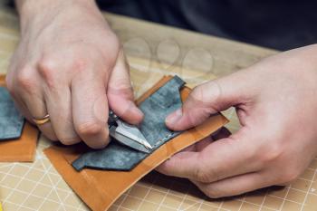 Man making leather wallet at a workshop. Concept of handmade craft production of leather goods.