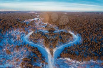 Aerial view of a heart shaped winter forest with frozen river