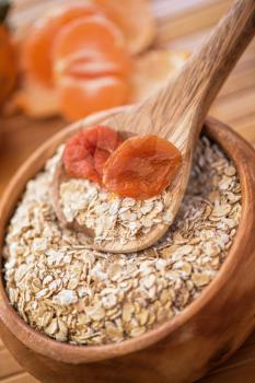 Oat flakes with  dried apricots at wooden plate on wooden background