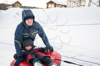 Father and his son having fun on a snow tube, at beauty winter day