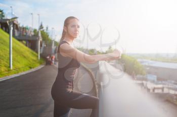 A woman in sportswear doing fitness exercises. City in sunny evening.