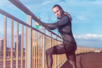 A woman in sportswear with bottle of water have rest at sunset on the evening city background