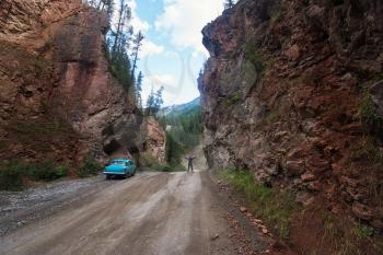 Woman and car on the road punched through the rocks in the Altai mountains, Siberia Russia