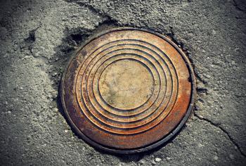 rusty round manhole on the broken asphalt