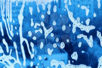 Blue background with natural soap foam pattern on the glass