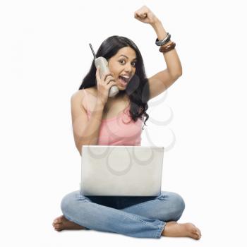 Young woman using a laptop and talking on a cordless phone