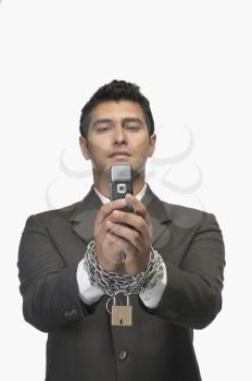 Businessman looking at a mobile phone with his hands in chains