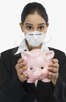 Businesswoman wearing an H1N1 mask and holding a piggy bank