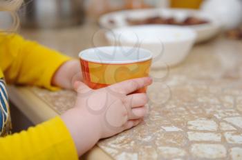 The hands of a small child hold a mug with water