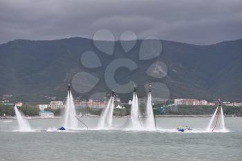 Beautiful show on the water, sports team fly on flyboards in the sea against the background of the mountains