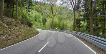 A highway through a forest with turns and a cyclist rides along it. Schwarzwald forest road and cyclist