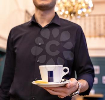 Waiter holding cup of coffee, tea at the restaurant