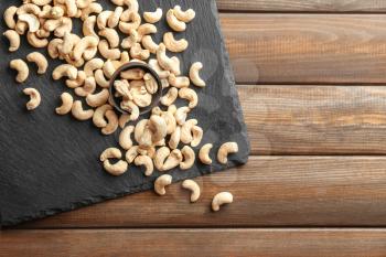 Slate plate and tasty cashew nuts on wooden background�