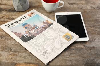 Newspaper with cup of tea and tablet computer on table�