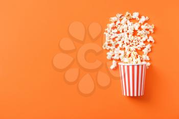 Paper bucket with scattered tasty popcorn on color background�