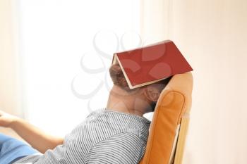 Young man sleeping with  book on his face at home�