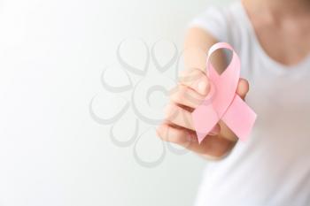Woman holding pink ribbon on light background, closeup. Breast cancer awareness concept�
