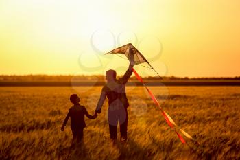 Happy father and son flying kite in the field at sunset�