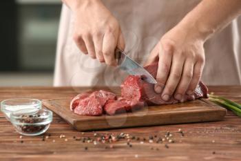 Man cutting raw meat on wooden board in kitchen�