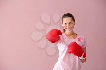 Beautiful woman with pink ribbon and boxing gloves on color background. Breast cancer concept�