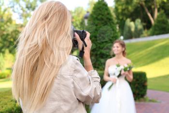 Professional photographer taking photo of beautiful bride outdoors�