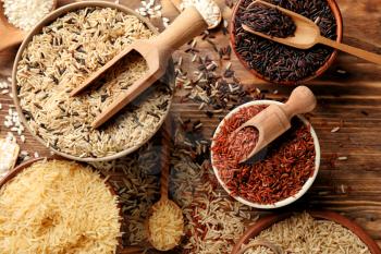 Different types of rice in bowls on wooden table�