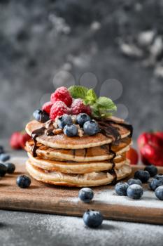 Wooden board with tasty homemade pancakes and berries on table�