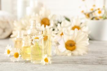 Bottles of essential oil with chamomile flowers on wooden table�