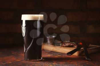 Glass of cold dark beer on color table�