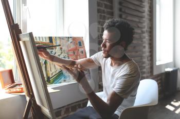 Young African-American artist painting picture in workshop�