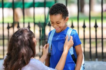 Mother helping her son to put on backpack outdoors�