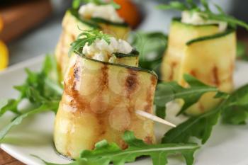 Tasty zucchini rolls with cheese and arugula on plate, closeup�