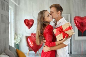 Young couple with gift box hugging at home�