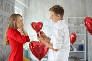 Young man proposing to his beloved with beautiful engagement ring at home�