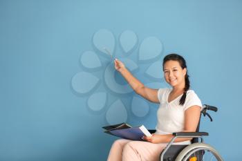 Female teacher in wheelchair showing something on color background�