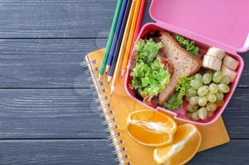 Lunch box with appetizing food and stationery on wooden table�