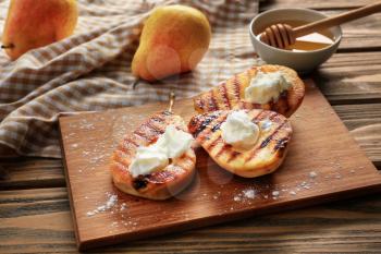 Halves of tasty grilled pears with ice cream on wooden board�