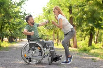 Man in wheelchair with beautiful woman dancing outdoors 