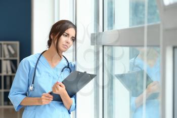 Tired female nurse near window in hospital�