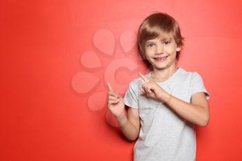 Little boy in t-shirt pointing at something on color background�
