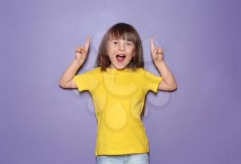 Little girl in t-shirt pointing at something on color background�
