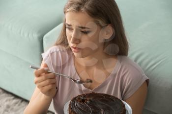 Lonely depressed woman eating chocolate cake at home�
